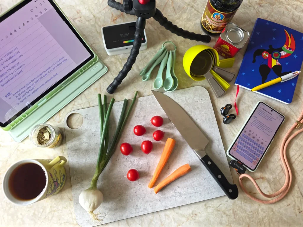 Behind the scenes: cooking ingredients, cutting board, tripod, lightbox, notebook, mobile devices, measuring cups, and tea.