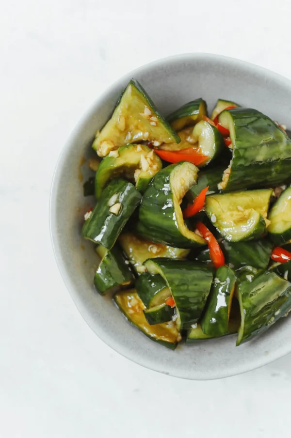 Smashed Cucumber Salad with red chilli in a white bowl on a marble table.