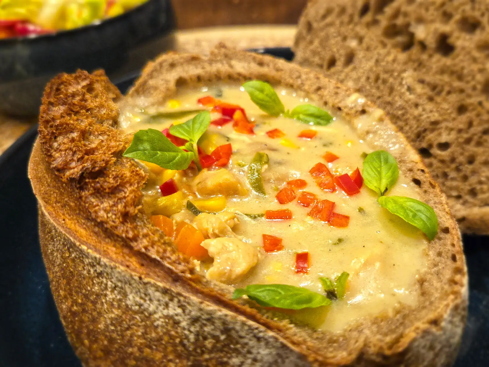 Creamy Thai chicken green curry chowder in a sourdough bread bowl, garnished with fresh basil and red bell pepper.