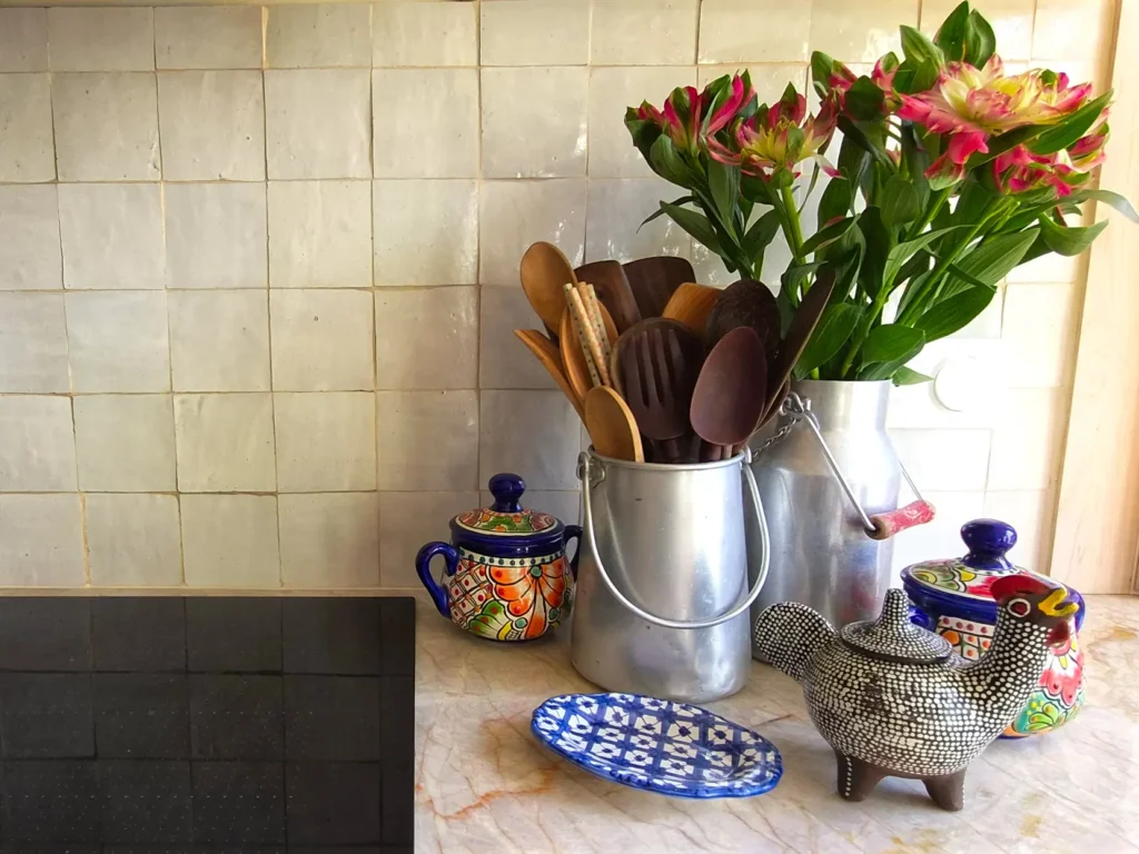 Zellige backdrop and marble kitchen counter with flowers, wooden utensils, Mexican spice jars, and artisan ceramic pieces.