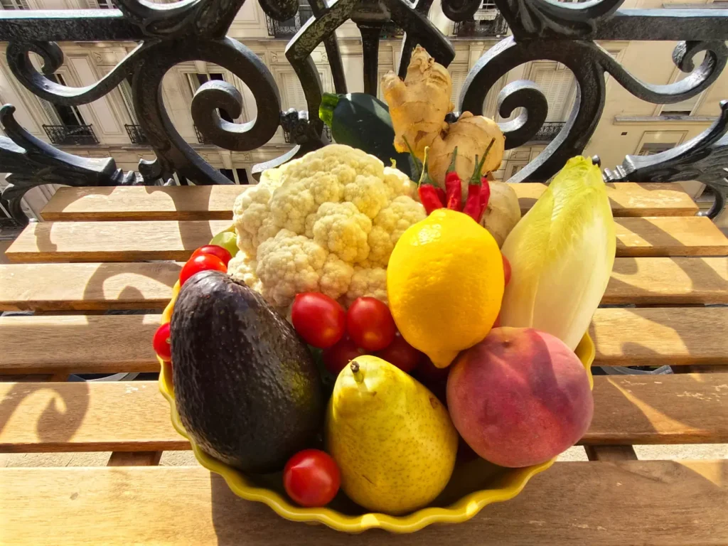 Pie dish of fresh produce on a sunny Parisian balcony: avocado, cauliflower, lemon, ginger, chili peppers, pear, and peach.
