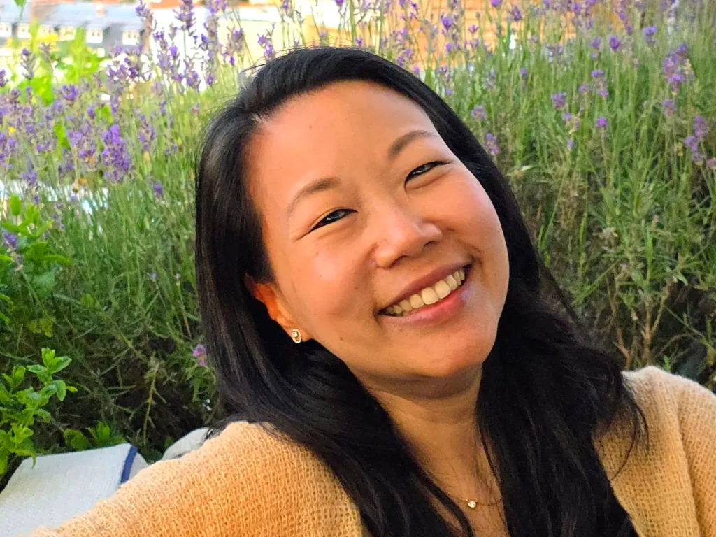 Nui smiling warmly on a Parisian rooftop with blooming Summer lavender in the background.
