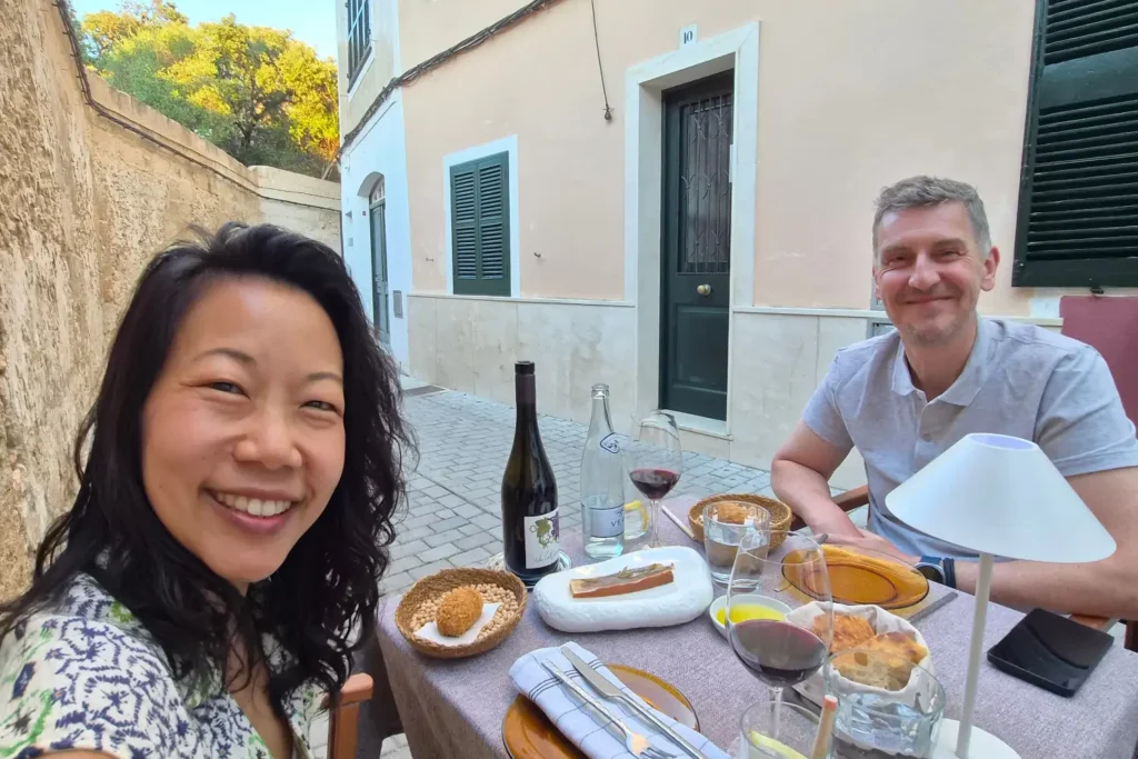 Nui and Nicolas enjoying a spectacular meal at Pez Limón restaurant in Menorca, on a street with a yellow flower tree.
