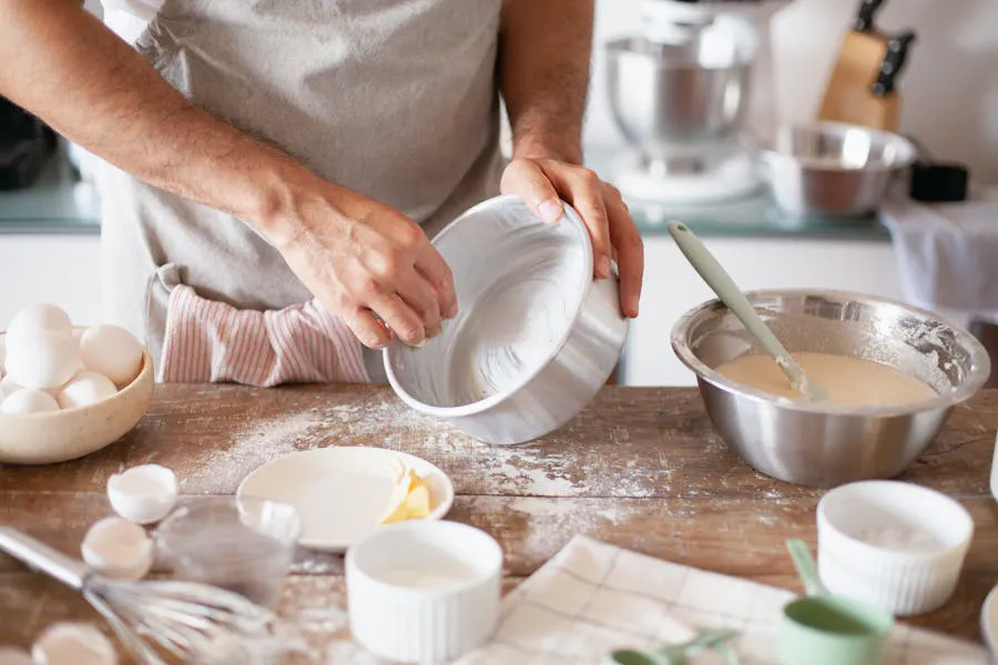 Baker greasing cake pan with butter, ingredients around. Baking preparation scene.