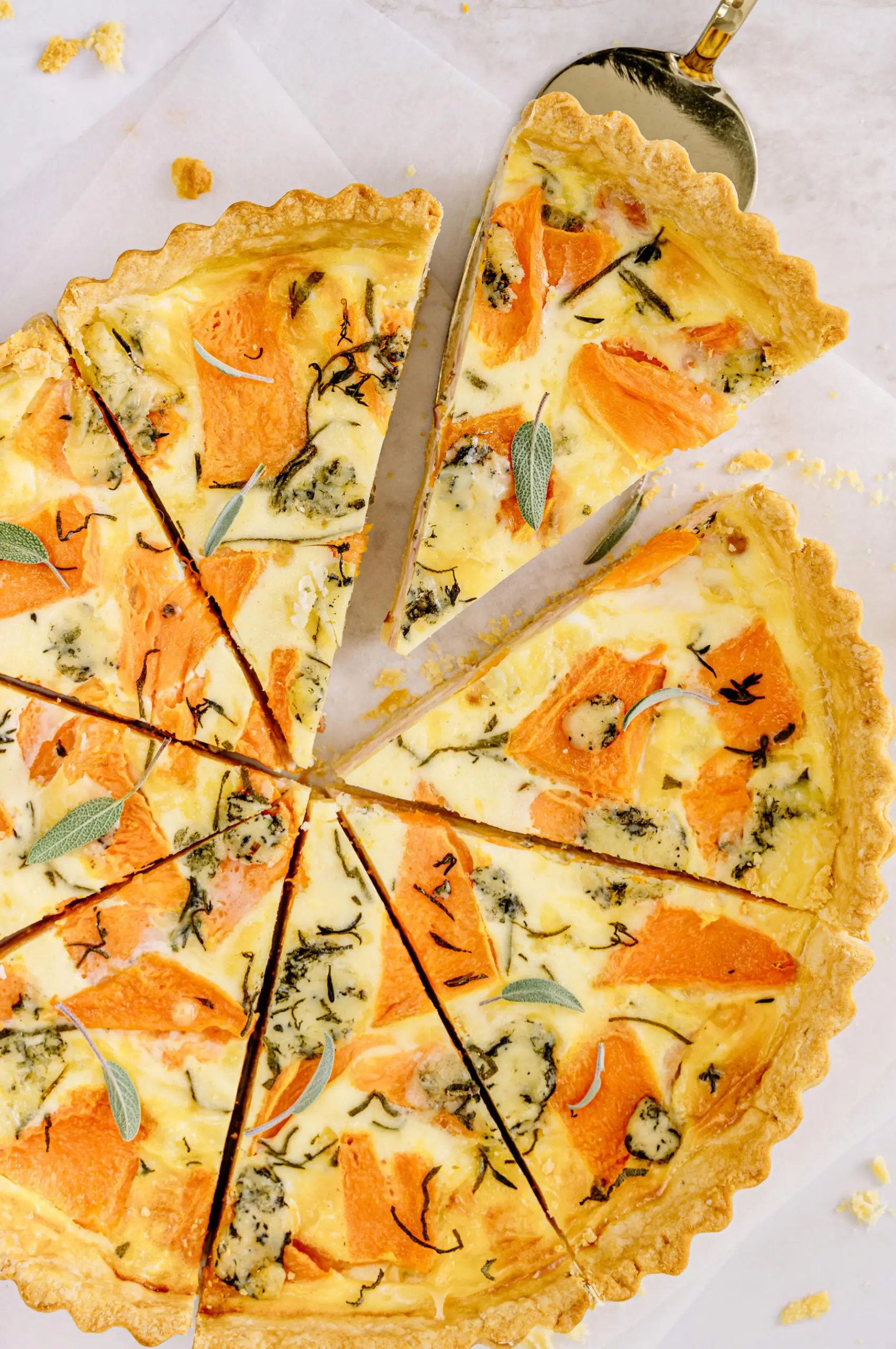 Butternut squash tart cut into slices with sage garnish.