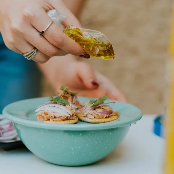 Crackers topped with meat and onion being drizzled with oil.