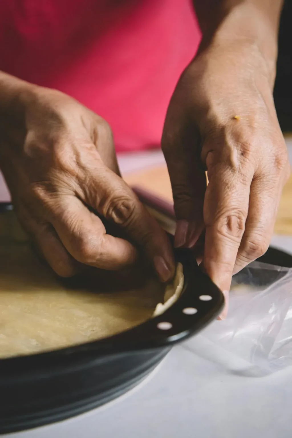 Hands crimping pie crust edge in baking pan, preparing homemade pie.