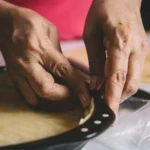 Hands crimping pie crust edge in baking pan, preparing homemade pie.