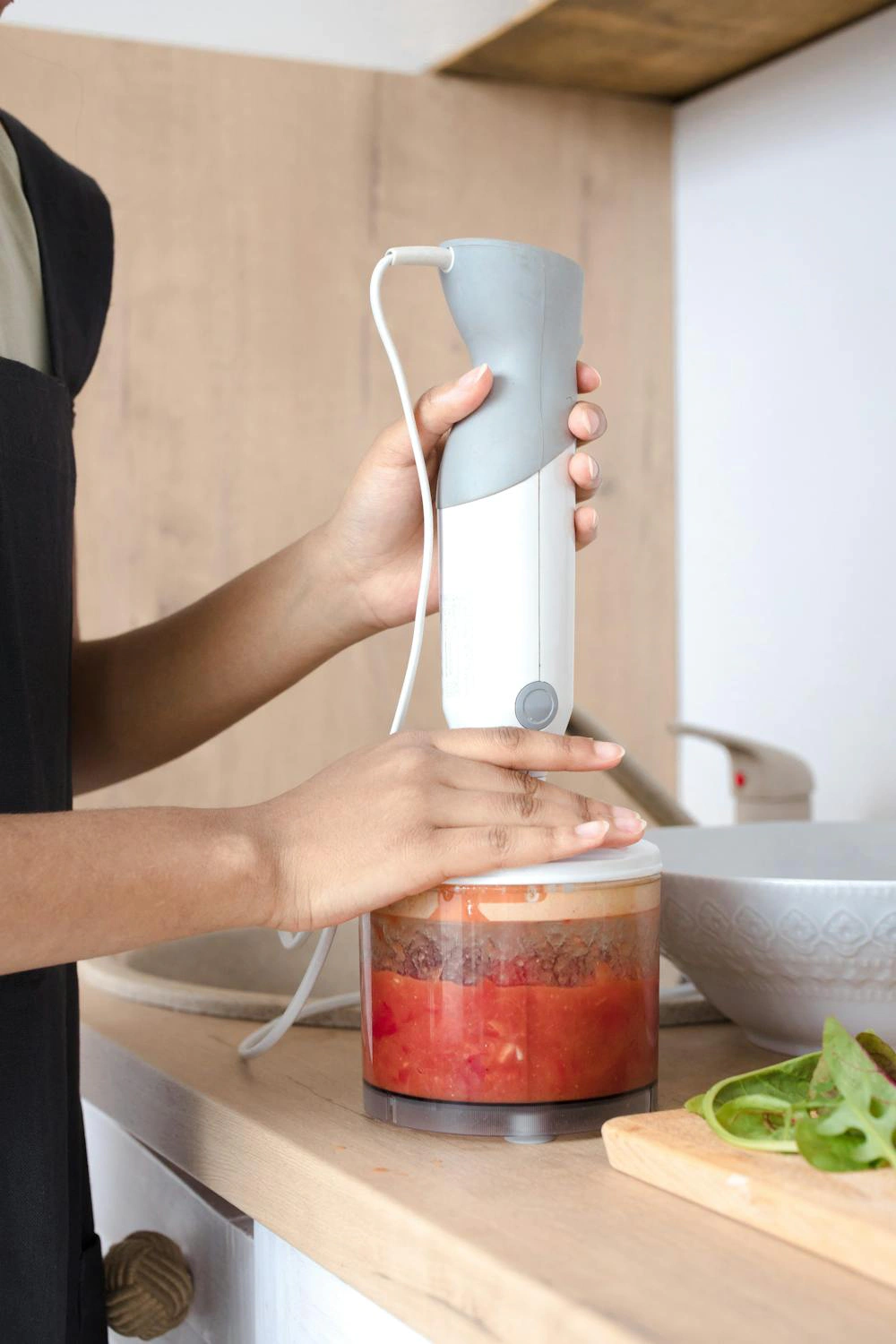 Person using immersion blender to blend tomato sauce in container.