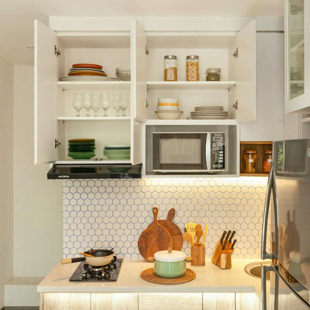 Modern kitchen with white cabinets, microwave, cookware, and blue hexagon backsplash.