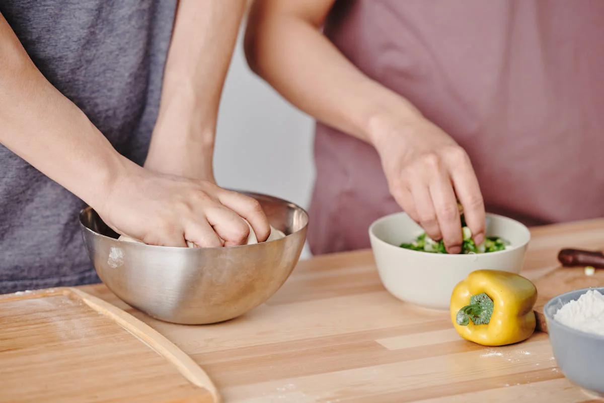 People preparing food together, kneading dough and chopping vegetables.