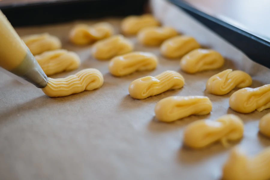 Piping dough for eclairs onto baking sheet with parchment paper.