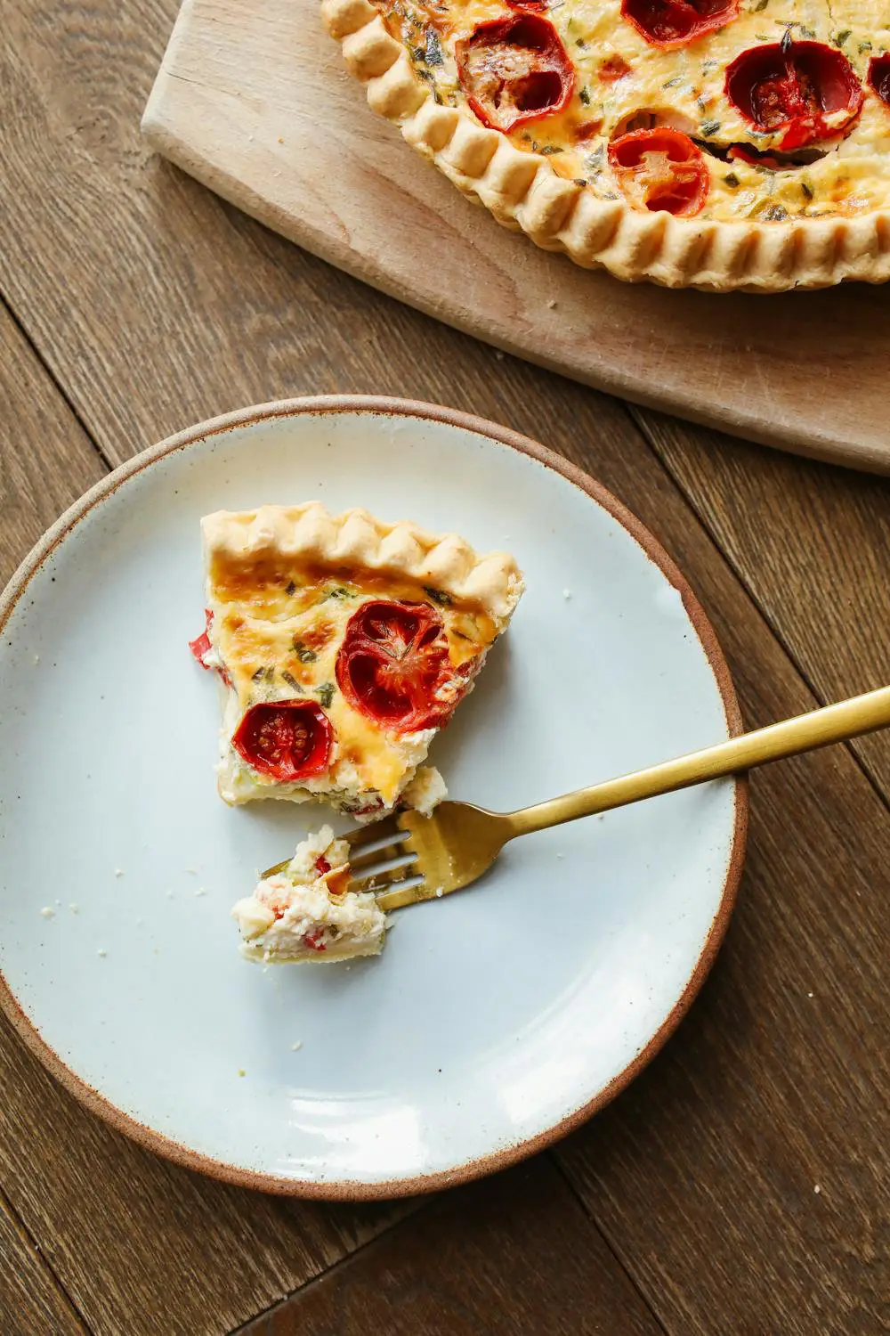 Slice of tomato quiche on plate with fork, wooden table.