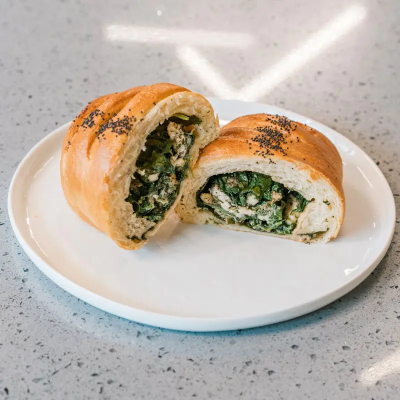 Sliced spinach and cheese roll on a white plate, close-up.