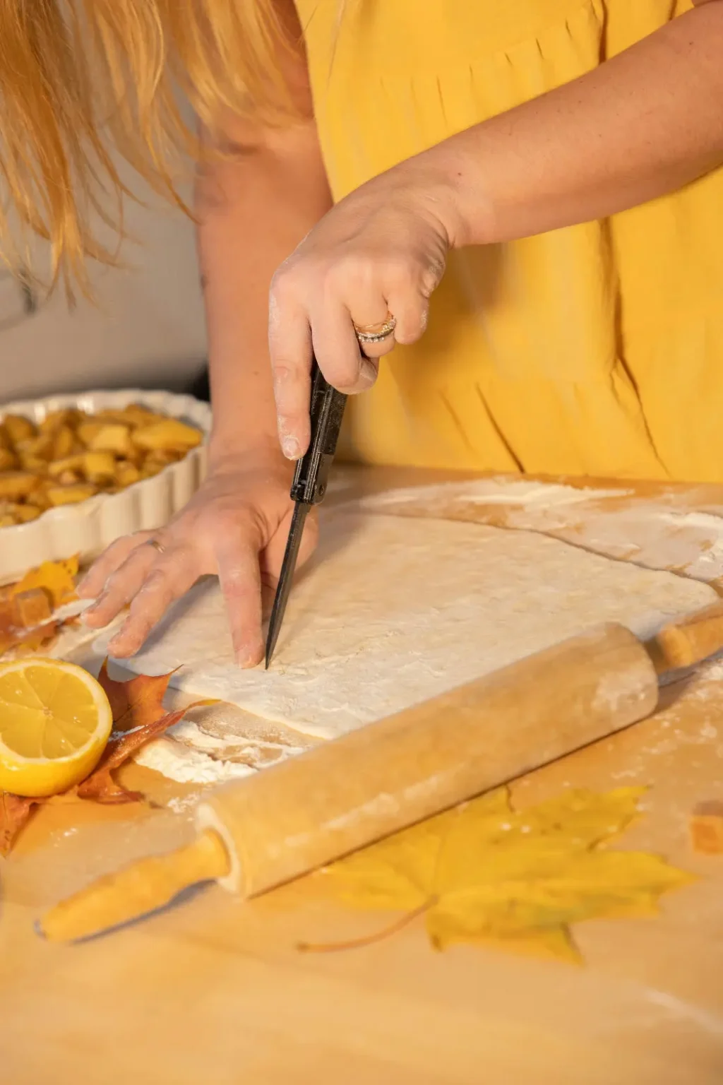 Woman cutting pie crust with knife, apple pie filling, fall leaves.