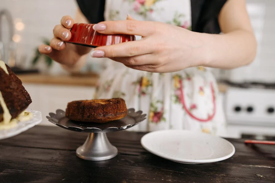 Woman plating a cake on a stand in a kitchen.